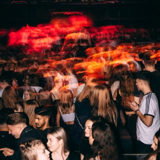 Een menigte jonge mensen in een nachtclub onder kleurrijke lichten, met beweging en energie overal.