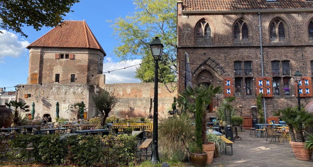 Buiten terras met stoelen en tafels tegen een achtergrond van een oude bakstenen muur en historisch gebouw.