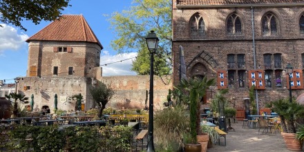 Buiten terras met stoelen en tafels tegen een achtergrond van een oude bakstenen muur en historisch gebouw.