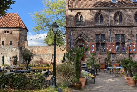 Buiten terras met stoelen en tafels tegen een achtergrond van een oude bakstenen muur en historisch gebouw.