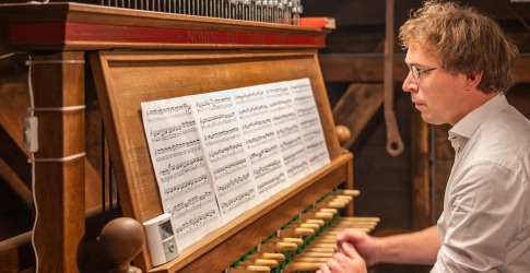 Een man speelt op een beiaardklavier met bladmuziek voor zich in een historische toren.