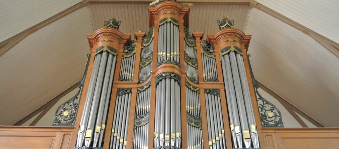 Pijporgel in een kerk, met houten omlijsting en gedetailleerde metalen versieringen aan het plafond.
