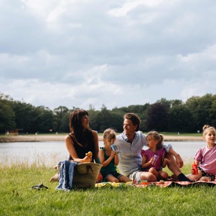 Gezin geniet van picknick aan het water, zittend op een deken met eten en drinken tijdens de zomer.