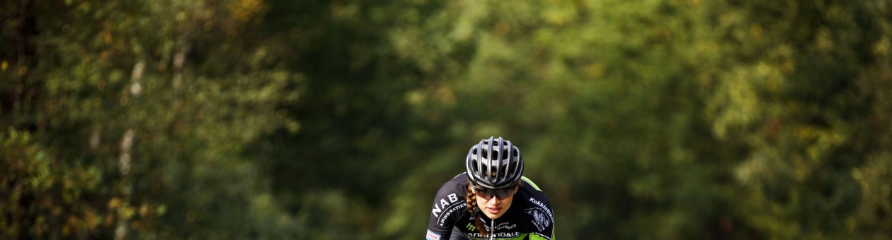 Wielrenner in wielertenue fietst snel op een rustige, bochtige weg omgeven door bomen en natuur.