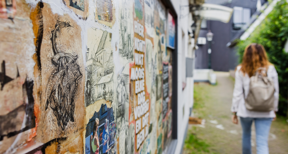 Vrouw loopt langs een muur met kleurrijke streetart en tekeningen in een smal steegje.