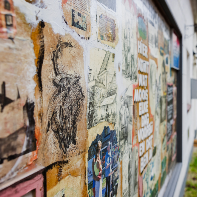 Frau geht an einer Wand mit bunter Streetart und Zeichnungen in einer schmalen Gasse vorbei.