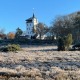 Een witte toren staat tussen bomen op de achtergrond, met een vorstig grasveld op een heldere winterdag.