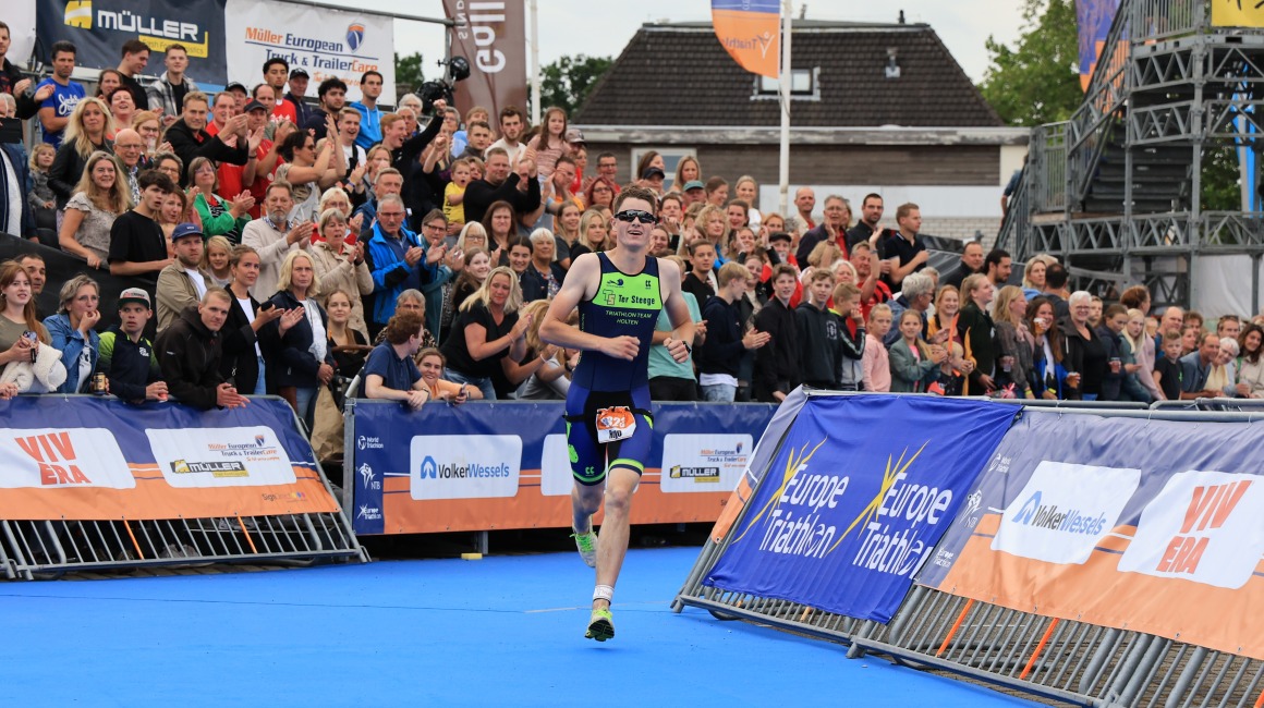 Triathlet läuft auf das Ziel zu, während jubelnde Zuschauer ihn bei einem sportlichen Wettkampf anfeuern.