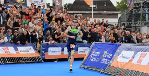 Triatleet rent naar de finish tijdens een wedstrijd met juichend publiek op de achtergrond in Nederland.