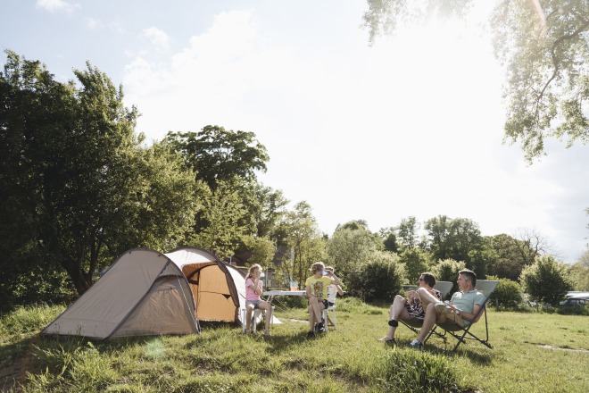 Gezin geniet van kamperen in de natuur met tent, stoelen en bomen op een zonnige dag in de zomer.