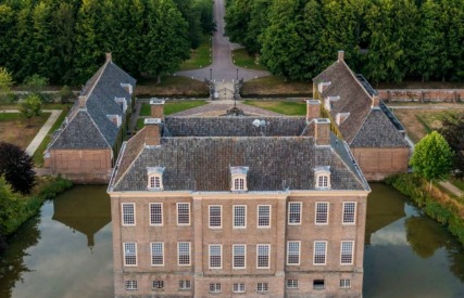Luchtfoto van een historisch kasteel met een gracht, omgeven door bomen en een oprijlaan in Nederland.