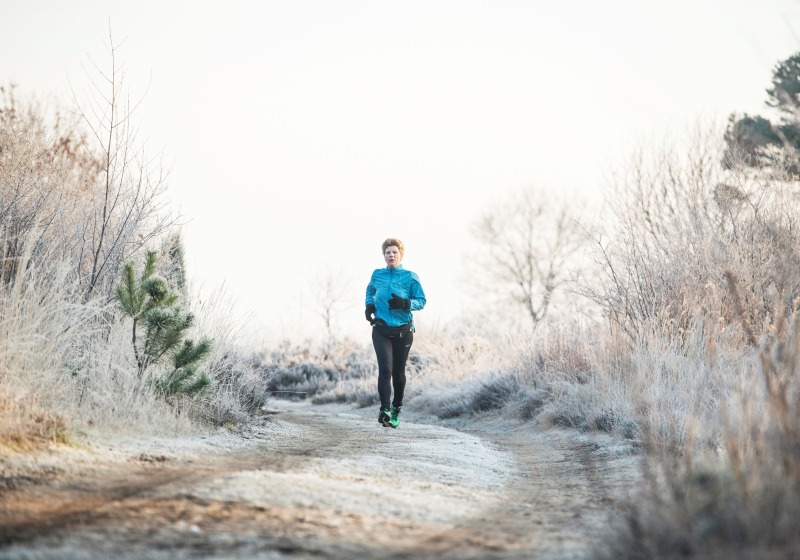 Persoon jogt op een winters, bevroren pad omgeven door kale bomen en struiken in een rustig landschap.