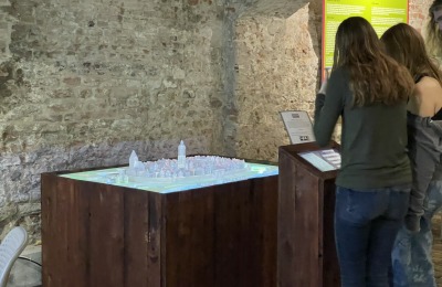 Twee vrouwen bekijken een maquette van een stadsexpositie in een ruimte met ruwe bakstenen muren.