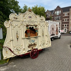 Een prachtig versierde Nederlandse draaiorgel, genaamd 'Pieperner', op straat naast een bestelwagen.
