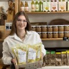 Vrouw in een winkel met lokaal voedsel, houdt een mand met mosterdsoep, potten pindakaas op de plank.