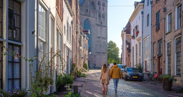 Stel loopt op een geplaveide straat in Nederland met oude huizen en een kerk op de achtergrond.