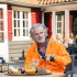 Older man in orange jacket enjoys outdoor dining at a patio table with bread, salad, and a drink.