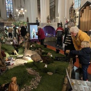 Bezoekers bekijken een uitgebreide kerststal met beelden en kunstgras in een kerk met glas-in-loodramen.