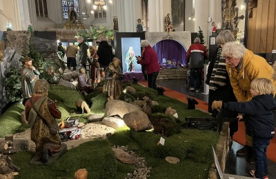 Bezoekers bekijken een uitgebreide kerststal met beelden en kunstgras in een kerk met glas-in-loodramen.