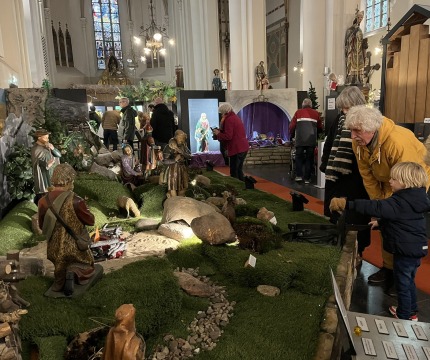 Bezoekers bekijken een uitgebreide kerststal met beelden en kunstgras in een kerk met glas-in-loodramen.