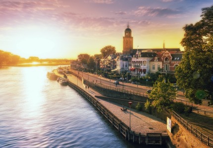 Zonsopgang boven een schilderachtig Nederlands stadje aan de rivier met historische gebouwen en toren.