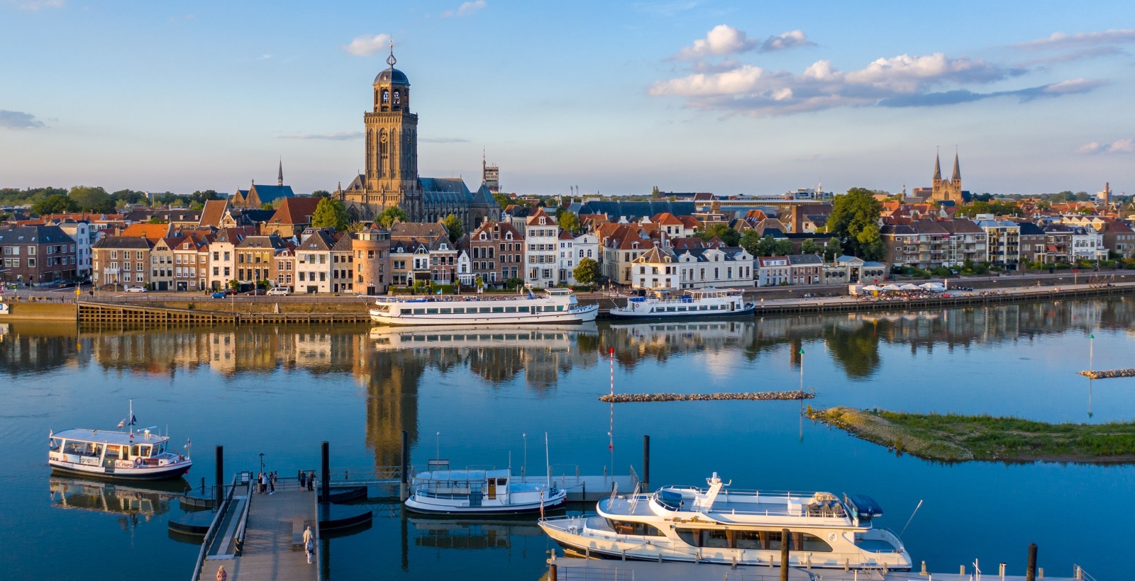 Uitzicht op de skyline van Deventer met de Lebuïnuskerk en boten op de IJssel bij zonnig weer.