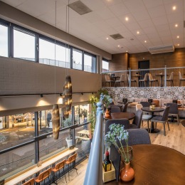 Modern ingericht café met gezellige zitplekken, grote ramen, warme verlichting en stijlvolle decoratie.