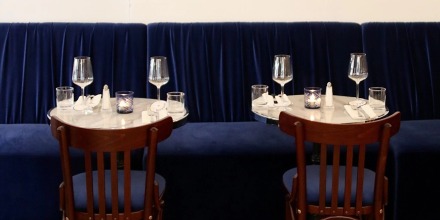 Two round tables with elegant glassware, wooden chairs, and a blue bench in a stylish restaurant setting.
