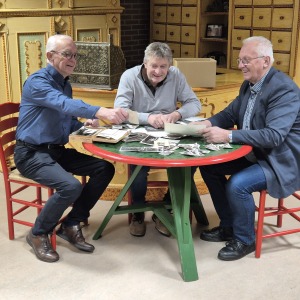 Drie oudere mannen zitten rond een tafel en bekijken samen oude foto's in een gezellige kamer.