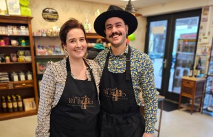 Twee lachende barista’s dragen zwarte schorten en staan samen in een gezellige koffiebar.