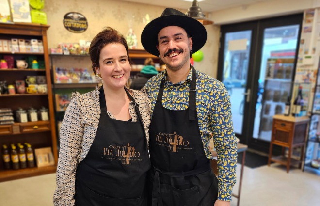 Twee lachende barista’s dragen zwarte schorten en staan samen in een gezellige koffiebar.