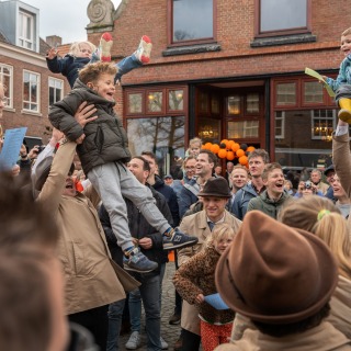 Een vrolijke menigte tilt kinderen op tijdens een feest op een plein met veel lachende gezichten.