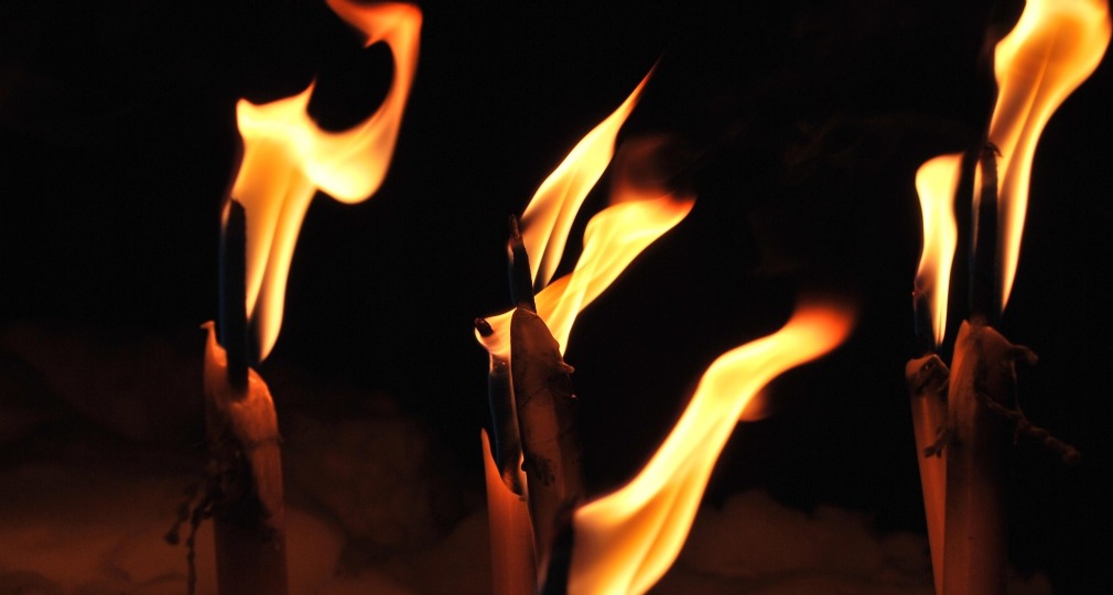 Verschillende brandende kaarsen met grote vlammen tegen een donkere achtergrond, sfeervol en warm.
