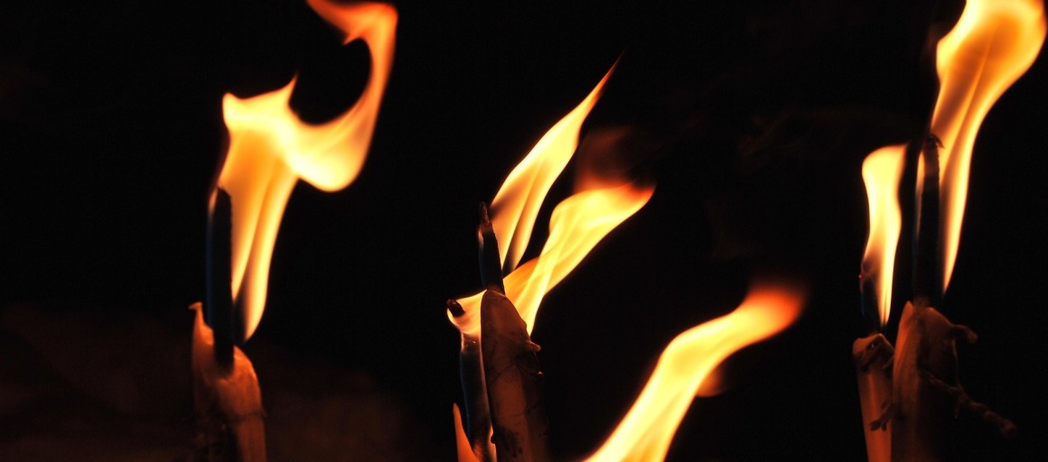 Verschillende brandende kaarsen met grote vlammen tegen een donkere achtergrond, sfeervol en warm.