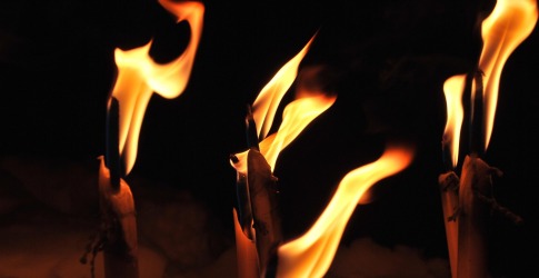 Verschillende brandende kaarsen met grote vlammen tegen een donkere achtergrond, sfeervol en warm.