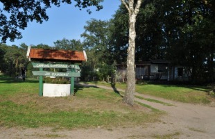 Eingang zum Campingplatz Kampeerboerderij De Zuurberg mit Holzschild, Sandweg und Bäumen im Hintergrund.