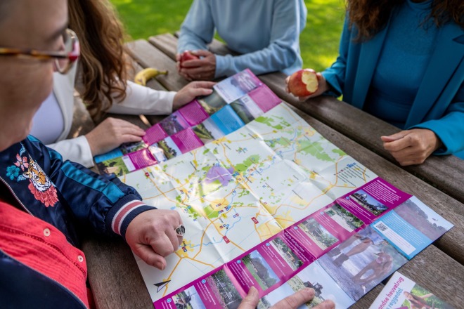 Vier mensen zitten aan een picknicktafel buiten, bekijken samen een uitgevouwen wandelkaart.