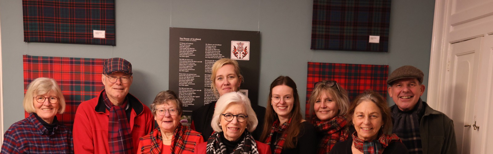 Groep lachende mensen poseren samen binnen voor rode en blauwe tartan stoffen aan de muur.