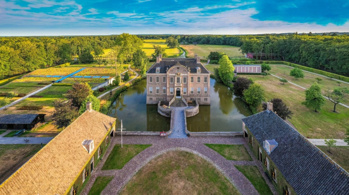 Luchtfoto van een historisch kasteel met slotgracht, symmetrische tuinen en omliggende natuur in Nederland.