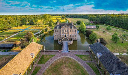 Luchtfoto van een historisch kasteel met slotgracht, symmetrische tuinen en omliggende natuur in Nederland.
