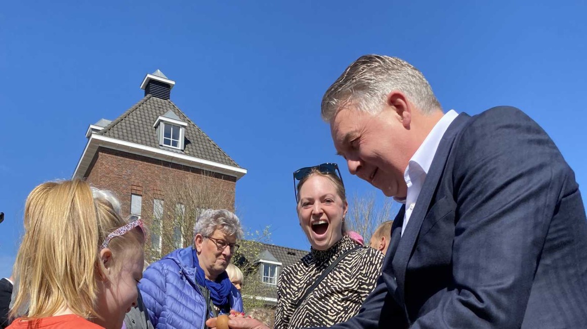 Mensen spelen een eitikkenspel buiten op een zonnige dag; een man en een meisje tikken eieren tegen elkaar.