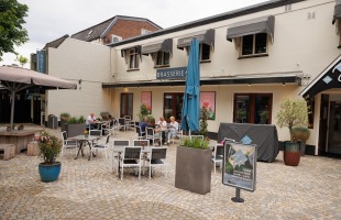 Buitenterras van een brasserie met stoelen, tafels en enkele etende gasten op een zonnige dag.