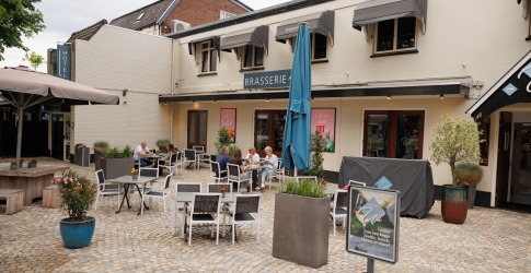 Buitenterras van een brasserie met stoelen, tafels en enkele etende gasten op een zonnige dag.