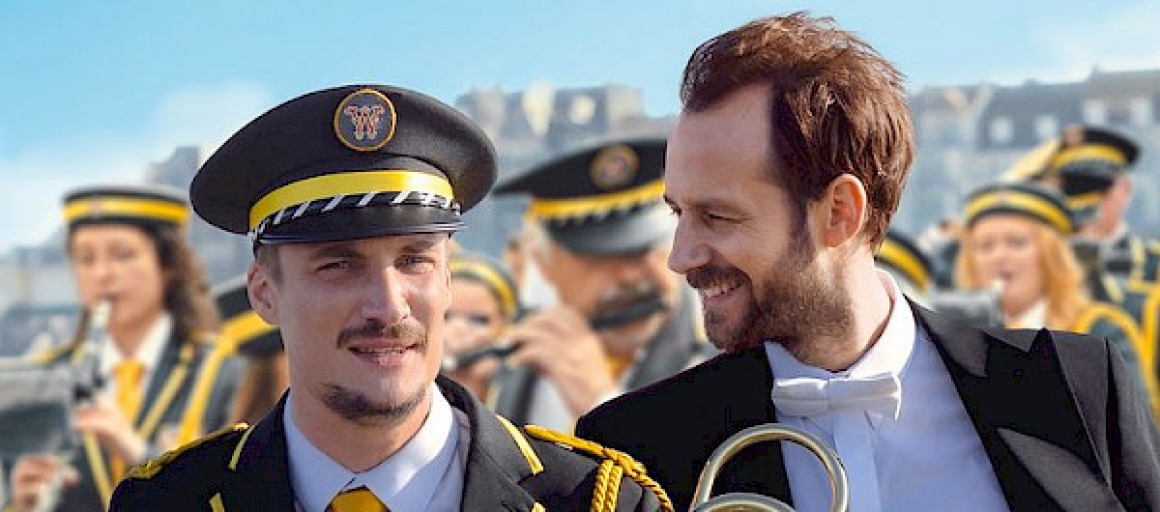 Film poster van 'En Fanfare' met twee mannen in orkestuniform en muziek, geregisseerd door Emmanuel Courcol.