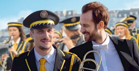 Film poster van 'En Fanfare' met twee mannen in orkestuniform en muziek, geregisseerd door Emmanuel Courcol.