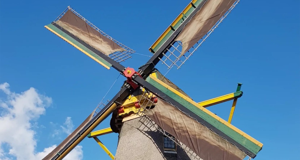 Een traditionele Nederlandse windmolen met rieten dak en grote wieken tegen een heldere blauwe lucht.