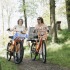 Twee vrouwen lopen met oranje fietsen door een groen bosrijk gebied op een zonnige dag in de natuur.