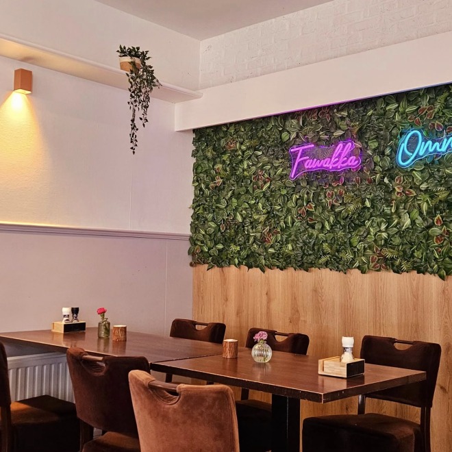 Gemütliches Café mit braunen Stühlen, Holztischen, Pflanzenwand und Neon-Schildern an der Wand.