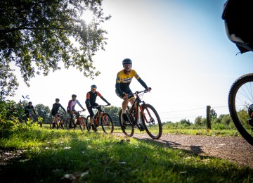 Groep fietsers rijdt op een zonnige dag over een landelijk pad, omringd door groen en veldhekken.