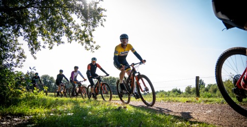Groep fietsers rijdt op een zonnige dag over een landelijk pad, omringd door groen en veldhekken.
